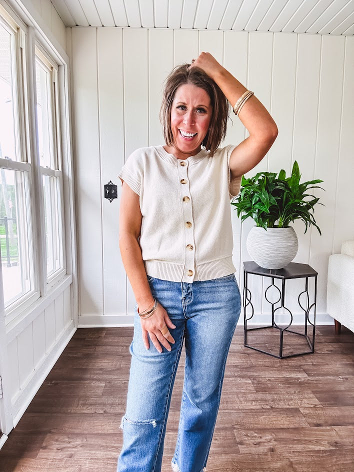 Soft, woven sweater vest with cap sleeves and faux wooden buttons down the front available in cream, sage and blush.