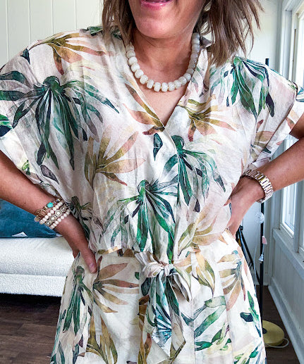 Lightweight and breezy set including a nearly sheer short sleeved tie front V neck top with cuffs at the sleeves and matching fully lined flowy skirt with elastic waist with flat front and pockets in beige with Earth toned tropical pattern.