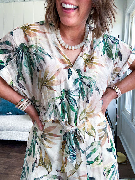 Lightweight and breezy set including a nearly sheer short sleeved tie front V neck top with cuffs at the sleeves and matching fully lined flowy skirt with elastic waist with flat front and pockets in beige with Earth toned tropical pattern.