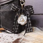 Black tweed fabric bow and black bow keychain with white floral and pearl charm on a lobster claw.