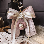 Pink tweed fabric bow and ivory bow keychain with pink and white floral and pearl charms on a lobster claw.