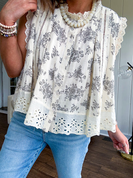 Thin, lightweight oversized cream button down sleeveless blouse with vintage inspired florals throughout and lace inserts and trim at the sleeves and hem.