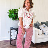 Thin, cotton linen blend cream top with short, puff sleeves, mock neck collar, red buttons down the front, a ruffle at the waist and red bow and floral embroidery throughout.