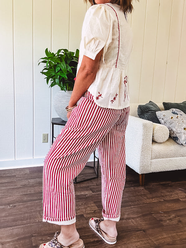 Thin, cotton linen blend cream top with short, puff sleeves, mock neck collar, red buttons down the front, a ruffle at the waist and red bow and floral embroidery throughout.