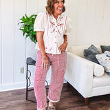 Thin, cotton linen blend cream top with short, puff sleeves, mock neck collar, red buttons down the front, a ruffle at the waist and red bow and floral embroidery throughout.