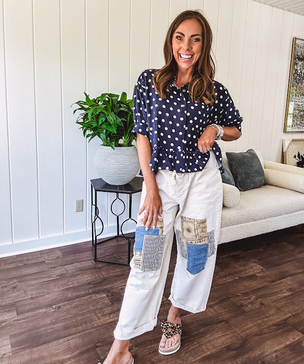 Thin, lightweight short sleeved button front top in navy with cream polka dots, a collar, front pocket, cuffed sleeves and a ruffled hem.