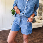 Thin, lightweight medium wash Chambray set featuring a long, tab sleeve top with collar and silver button down front with front pockets and matching elastic drawstring waist shorts with side pockets.