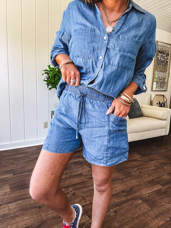Thin, lightweight medium wash Chambray set featuring a long, tab sleeve top with collar and silver button down front with front pockets and matching elastic drawstring waist shorts with side pockets.
