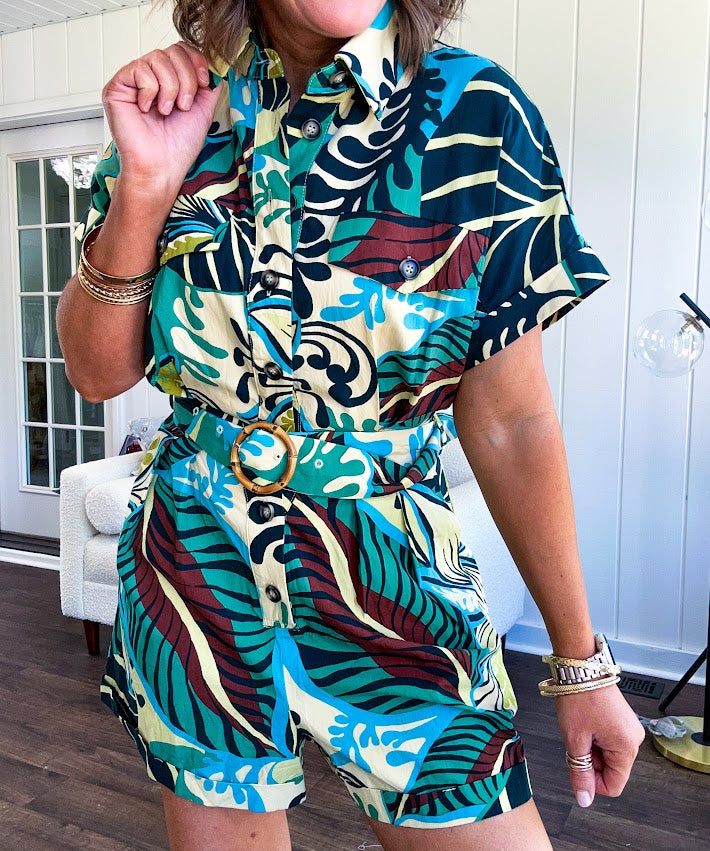Welcome to the jungle in this bold rainforest-inspired print romper that commands attention. Crafted in rich earth tones, it features a button down front and two buttoned front pockets, a classic collar, and a matching fabric belt that cinches your silhouette. The relaxed design flows effortlessly, and yes—it has pockets