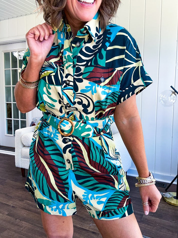Welcome to the jungle in this bold rainforest-inspired print romper that commands attention. Crafted in rich earth tones, it features a button down front and two buttoned front pockets, a classic collar, and a matching fabric belt that cinches your silhouette. The relaxed design flows effortlessly, and yes—it has pockets
