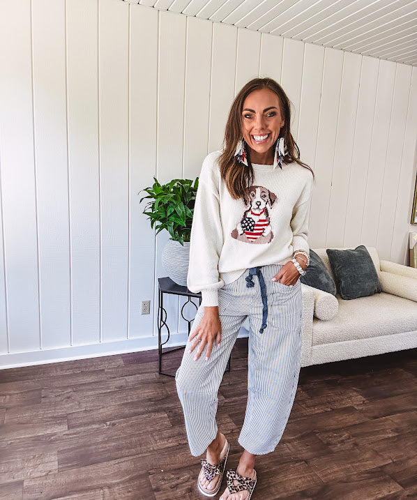 Cream knit long sleeved sweater with round neck and dog motif holding an American flag heart.