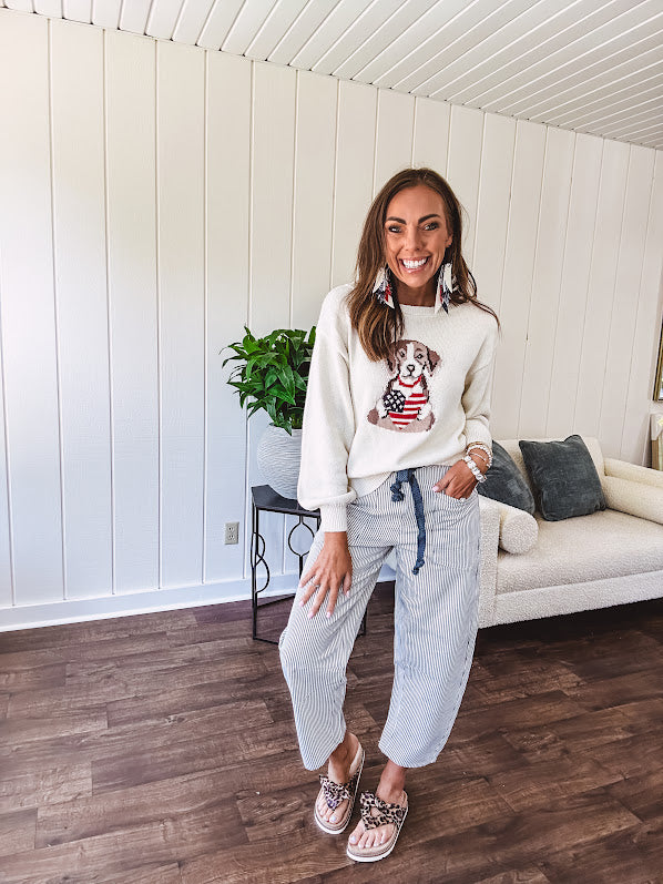 Cream knit long sleeved sweater with round neck and dog motif holding an American flag heart.
