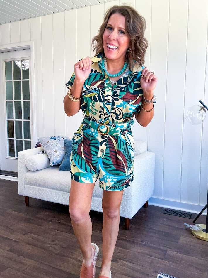 Welcome to the jungle in this bold rainforest-inspired print romper that commands attention. Crafted in rich earth tones, it features a button down front and two buttoned front pockets, a classic collar, and a matching fabric belt that cinches your silhouette. The relaxed design flows effortlessly, and yes—it has pockets