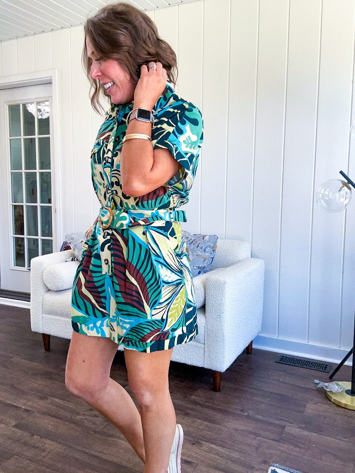 Welcome to the jungle in this bold rainforest-inspired print romper that commands attention. Crafted in rich earth tones, it features a button down front and two buttoned front pockets, a classic collar, and a matching fabric belt that cinches your silhouette. The relaxed design flows effortlessly, and yes—it has pockets