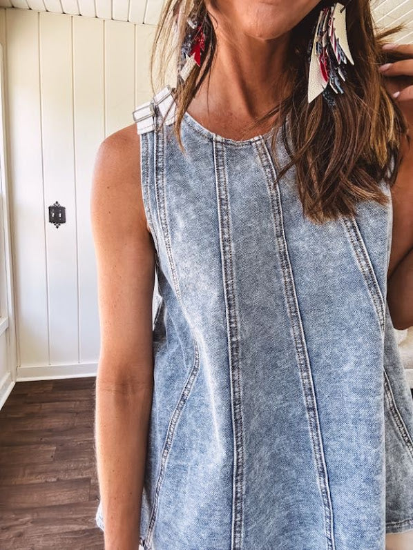 Stretchy medium washed denim tank with canvas adjustable straps at the shoulders and a wide hem with vertical seams throughout.