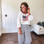 Cream long sleeved sweater with round neck and red trim at neck an cuffs with American Flag motif.