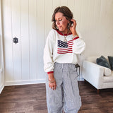 Cream long sleeved sweater with round neck and red trim at neck an cuffs with American Flag motif.