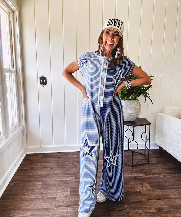 Soft terry-like cotton jumpsuit in indigo and light blue stripes with star patches throughout with lace embellishments. Wide lg design and faux wooden buttons down the front.