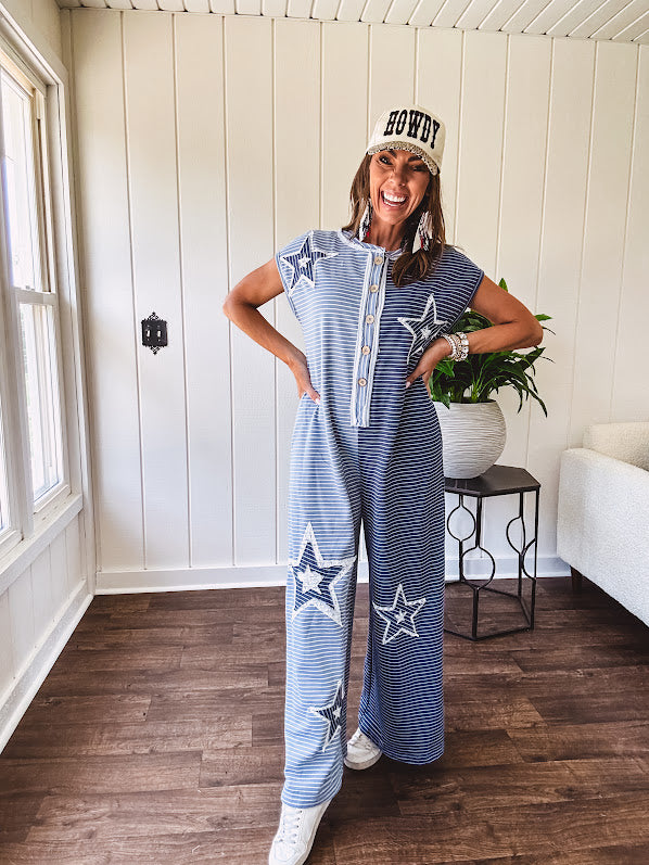 Soft terry-like cotton jumpsuit in indigo and light blue stripes with star patches throughout with lace embellishments. Wide lg design and faux wooden buttons down the front.