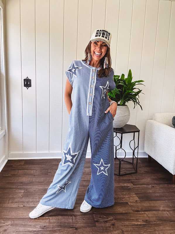 Soft terry-like cotton jumpsuit in indigo and light blue stripes with star patches throughout with lace embellishments. Wide lg design and faux wooden buttons down the front.