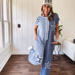 Soft terry-like cotton jumpsuit in indigo and light blue stripes with star patches throughout with lace embellishments. Wide lg design and faux wooden buttons down the front.