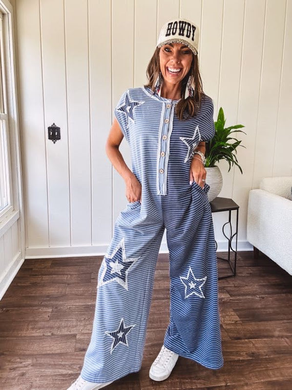 Soft terry-like cotton jumpsuit in indigo and light blue stripes with star patches throughout with lace embellishments. Wide lg design and faux wooden buttons down the front.