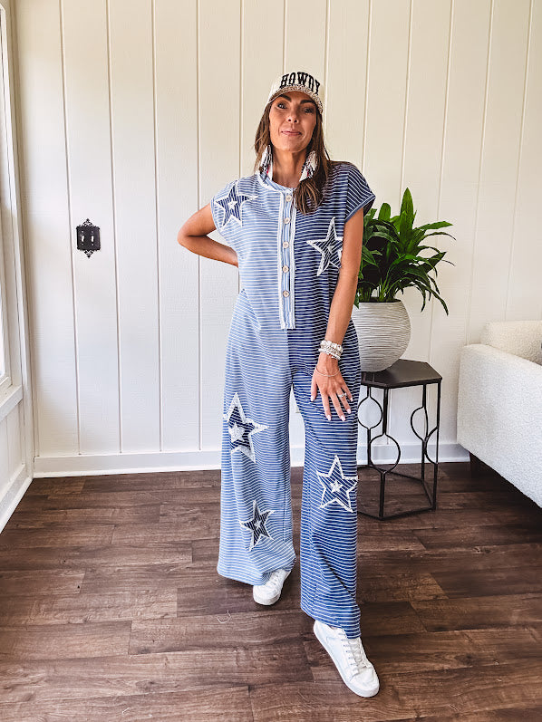 Soft terry-like cotton jumpsuit in indigo and light blue stripes with star patches throughout with lace embellishments. Wide lg design and faux wooden buttons down the front.