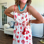 This fully lined white midi features an eye-catching red shell print that demands attention, paired with adjustable red spaghetti straps and a show-stopping red and white striped rope belt complete with charming tassels.