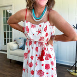 This fully lined white midi features an eye-catching red shell print that demands attention, paired with adjustable red spaghetti straps and a show-stopping red and white striped rope belt complete with charming tassels.