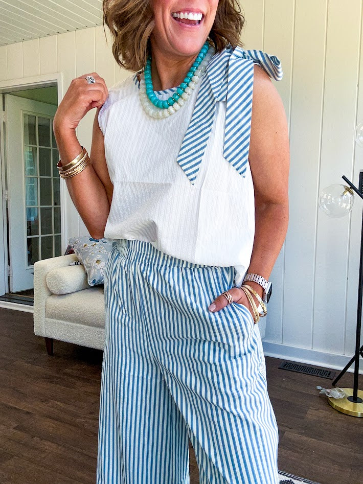 The lightweight cream tank features a playful blue and white striped bow at the shoulder and matching trim around the round neckline, finished with a hook and eye closure. Pair it with the coordinating wide-leg pants, complete with pockets and that same breezy stripe detail at the waist.