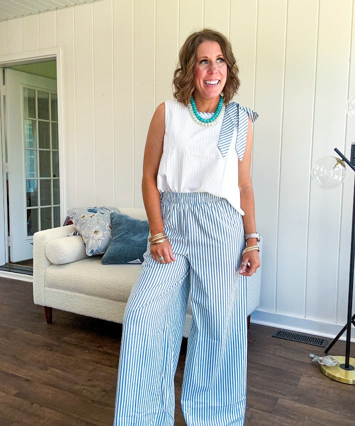 The lightweight cream tank features a playful blue and white striped bow at the shoulder and matching trim around the round neckline, finished with a hook and eye closure. Pair it with the coordinating wide-leg pants, complete with pockets and that same breezy stripe detail at the waist.