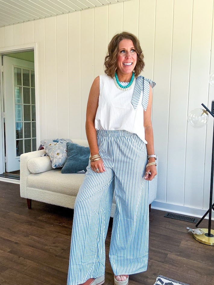 The lightweight cream tank features a playful blue and white striped bow at the shoulder and matching trim around the round neckline, finished with a hook and eye closure. Pair it with the coordinating wide-leg pants, complete with pockets and that same breezy stripe detail at the waist.