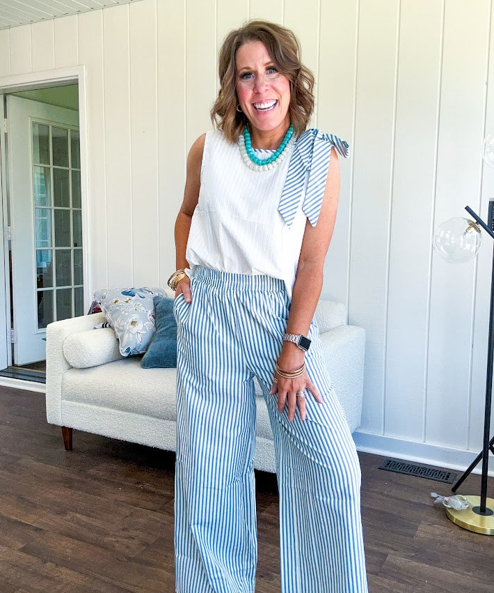 The lightweight cream tank features a playful blue and white striped bow at the shoulder and matching trim around the round neckline, finished with a hook and eye closure. Pair it with the coordinating wide-leg pants, complete with pockets and that same breezy stripe detail at the waist.