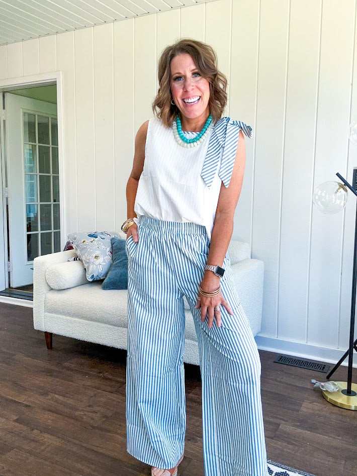 The lightweight cream tank features a playful blue and white striped bow at the shoulder and matching trim around the round neckline, finished with a hook and eye closure. Pair it with the coordinating wide-leg pants, complete with pockets and that same breezy stripe detail at the waist.