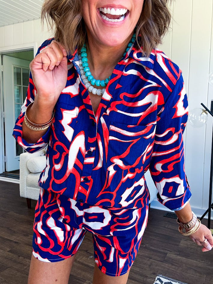 Soft, lightweight set featuring a 3/4 tab sleeve top with button down front and collar with matching elastic waist shorts with front pleats and pockets as well as lining in a bold navy, orange and white modern print.