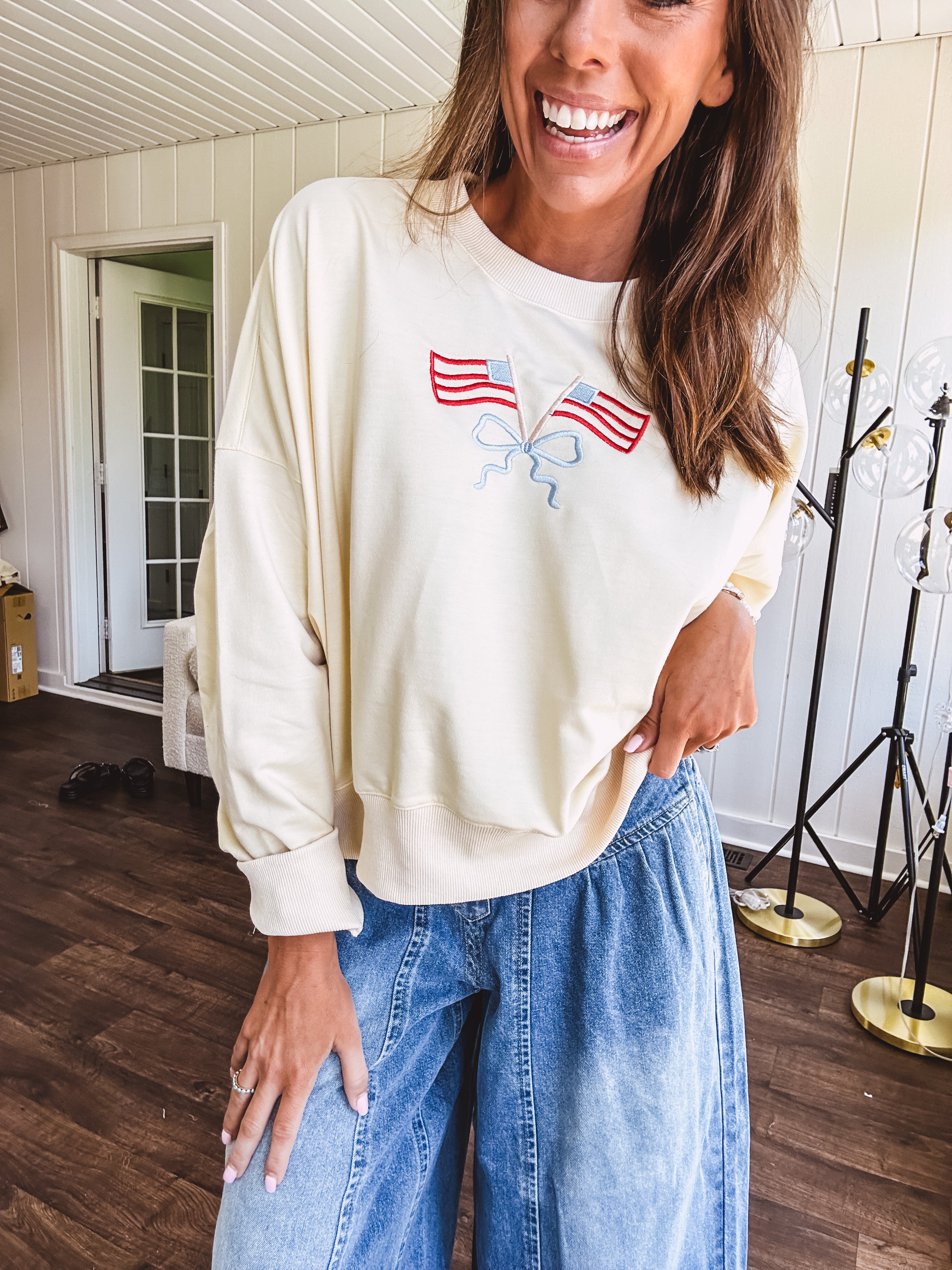 Cropped creamy light weight crew pullover with long sleeves and American flag embroidery with a light blue bow on the front.