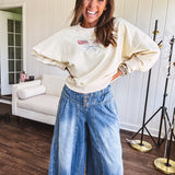 Cropped creamy light weight crew pullover with long sleeves and American flag embroidery with a light blue bow on the front.
