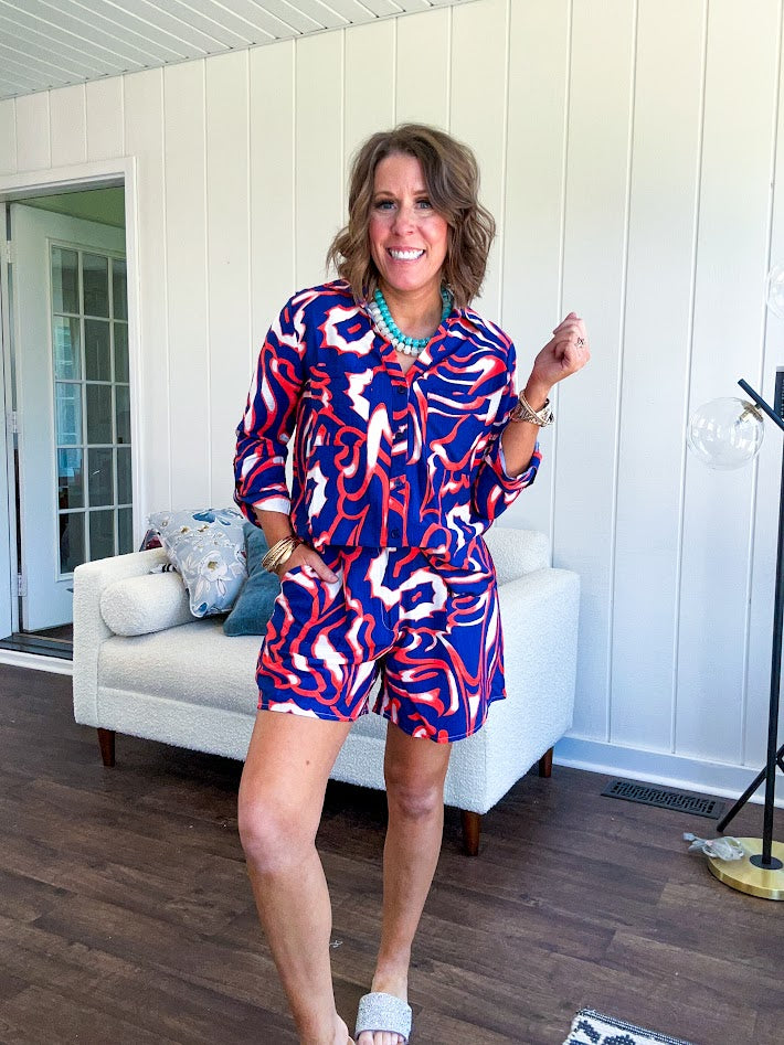 Soft, lightweight set featuring a 3/4 tab sleeve top with button down front and collar with matching elastic waist shorts with front pleats and pockets as well as lining in a bold navy, orange and white modern print.