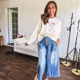 Cropped creamy light weight crew pullover with long sleeves and American flag embroidery with a light blue bow on the front.