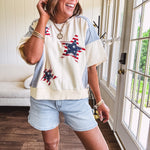 Cream short sleeved terry-like top with light blue inserts on shoulders and down sides with red and white stripe and denim blue star patches on the front.