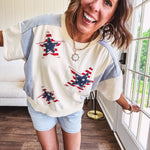Cream short sleeved terry-like top with light blue inserts on shoulders and down sides with red and white stripe and denim blue star patches on the front.