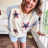 Cream short sleeved terry-like top with light blue inserts on shoulders and down sides with red and white stripe and denim blue star patches on the front.