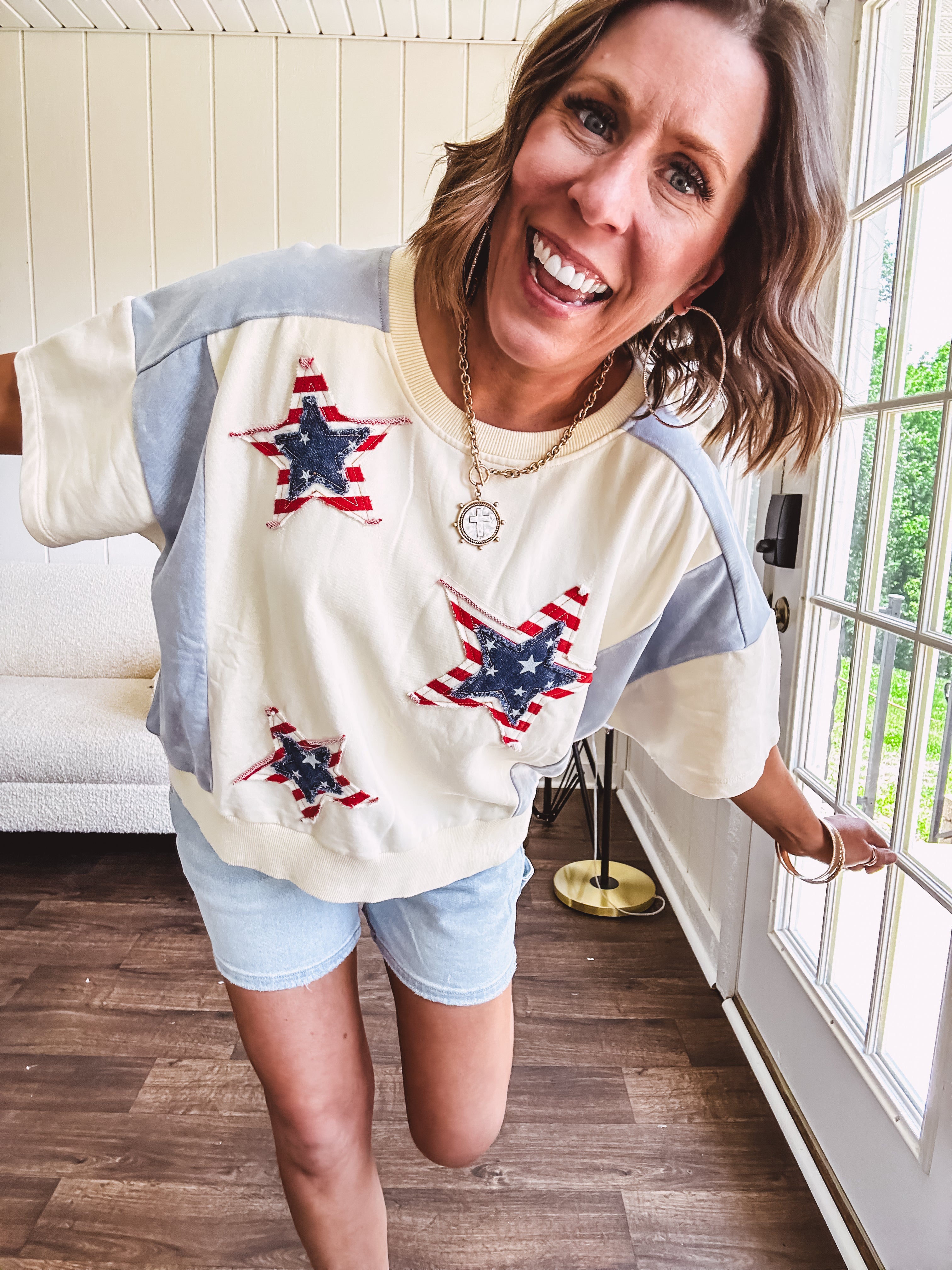 Cream short sleeved terry-like top with light blue inserts on shoulders and down sides with red and white stripe and denim blue star patches on the front.