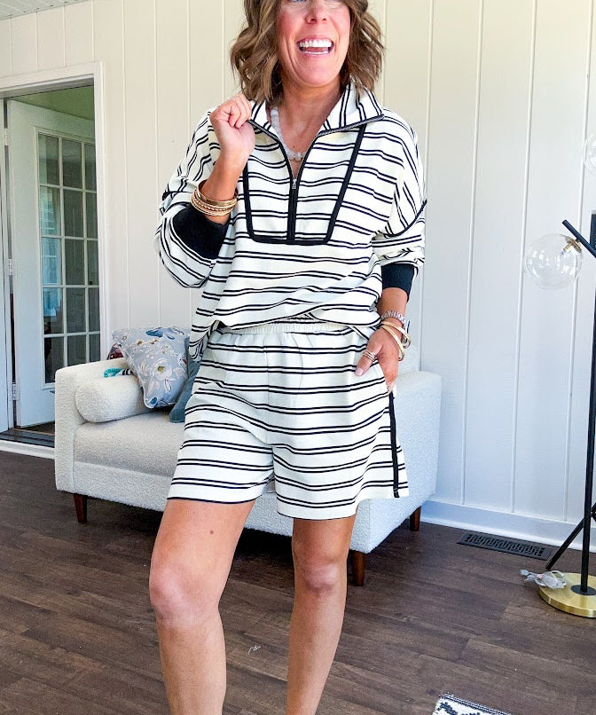 Lightweight cream and black striped set with 1/4 zip and collar top with black trim at the yoke and cuffs on the long sleeves and matching elastic waist shorts with pockets and black trim down the sides.