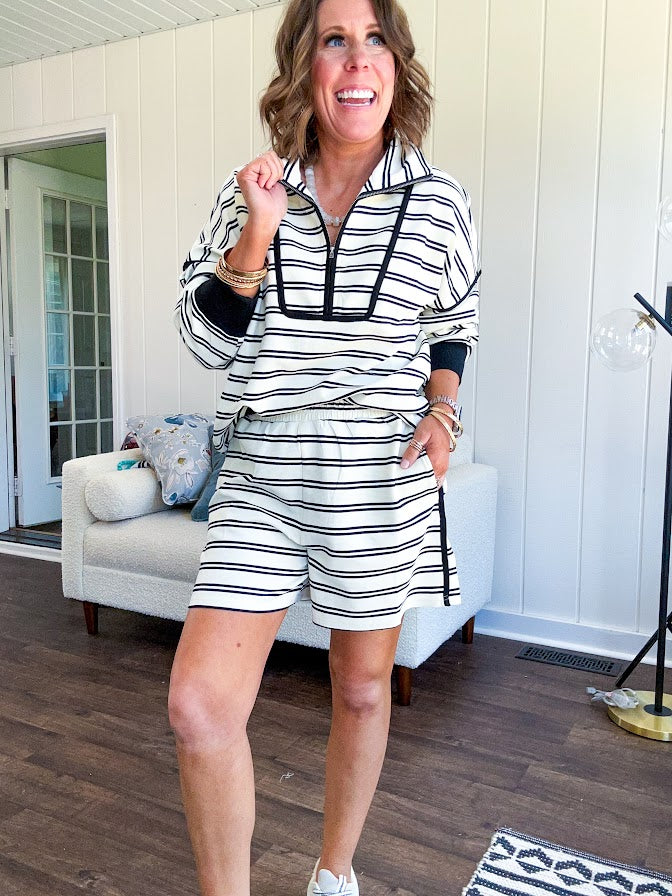 Lightweight cream and black striped set with 1/4 zip and collar top with black trim at the yoke and cuffs on the long sleeves and matching elastic waist shorts with pockets and black trim down the sides.