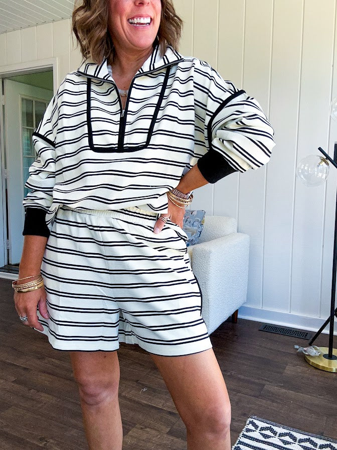 Lightweight cream and black striped set with 1/4 zip and collar top with black trim at the yoke and cuffs on the long sleeves and matching elastic waist shorts with pockets and black trim down the sides.