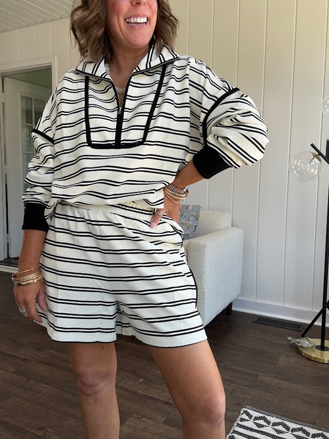 Lightweight cream and black striped set with 1/4 zip and collar top with black trim at the yoke and cuffs on the long sleeves and matching elastic waist shorts with pockets and black trim down the sides.