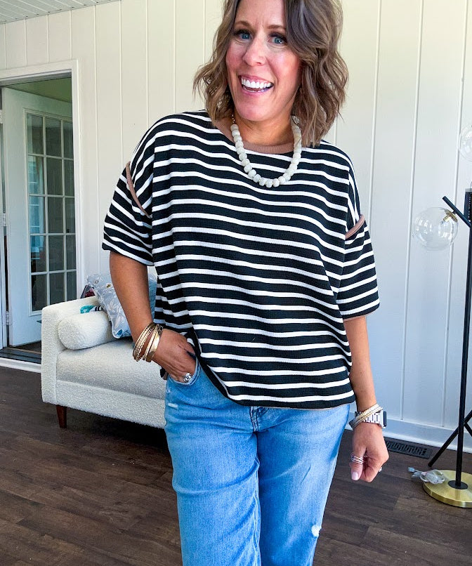 Soft, lightweight stretchy fabric in stripes including black and white, cream and white with contrasting trim at the round neck, hemline and sleeves. short sleeved and boxy cut.