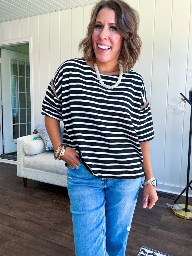 Soft, lightweight stretchy fabric in stripes including black and white, cream and white with contrasting trim at the round neck, hemline and sleeves. short sleeved and boxy cut.