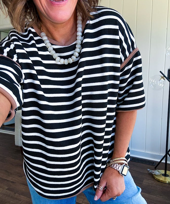 Soft, lightweight stretchy fabric in stripes including black and white, cream and white with contrasting trim at the round neck, hemline and sleeves. short sleeved and boxy cut.